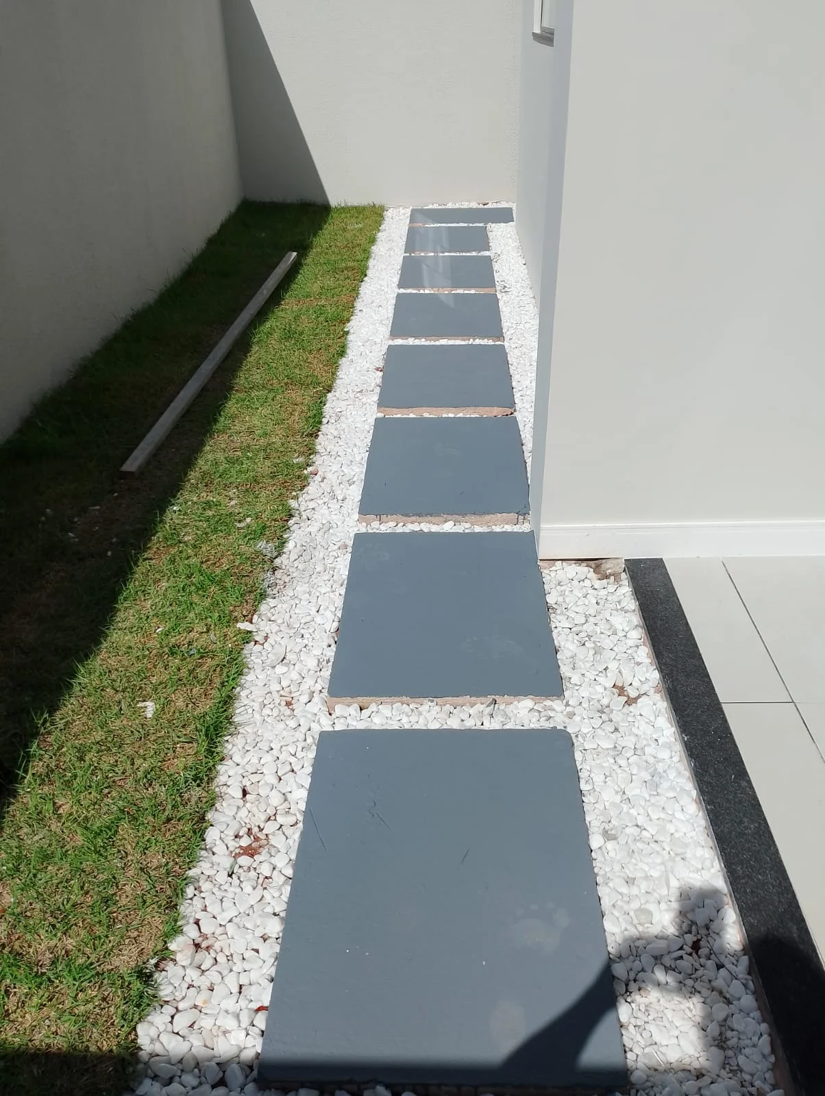 Passeio lateral em placas de concreto sobre pedra branca, com grama nas laterais