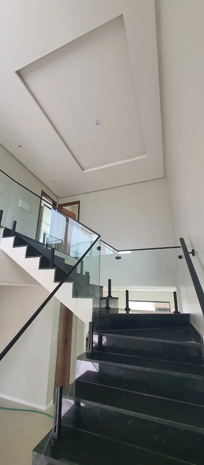 Escada em granito preto com guarda-corpo de vidro, vista da sala