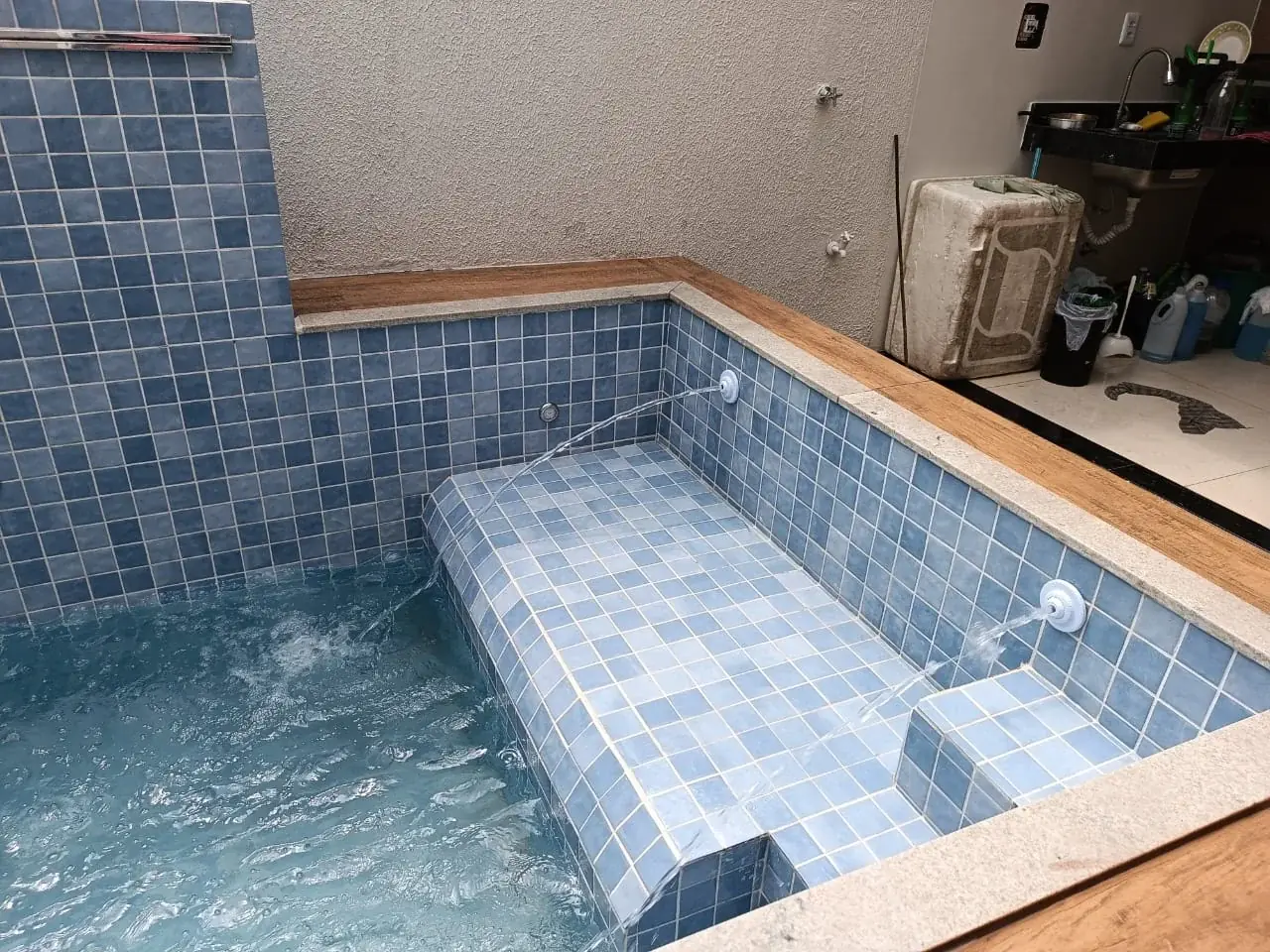 Piscina revestida em pastilha azul com deck em porcelanato amadeirado