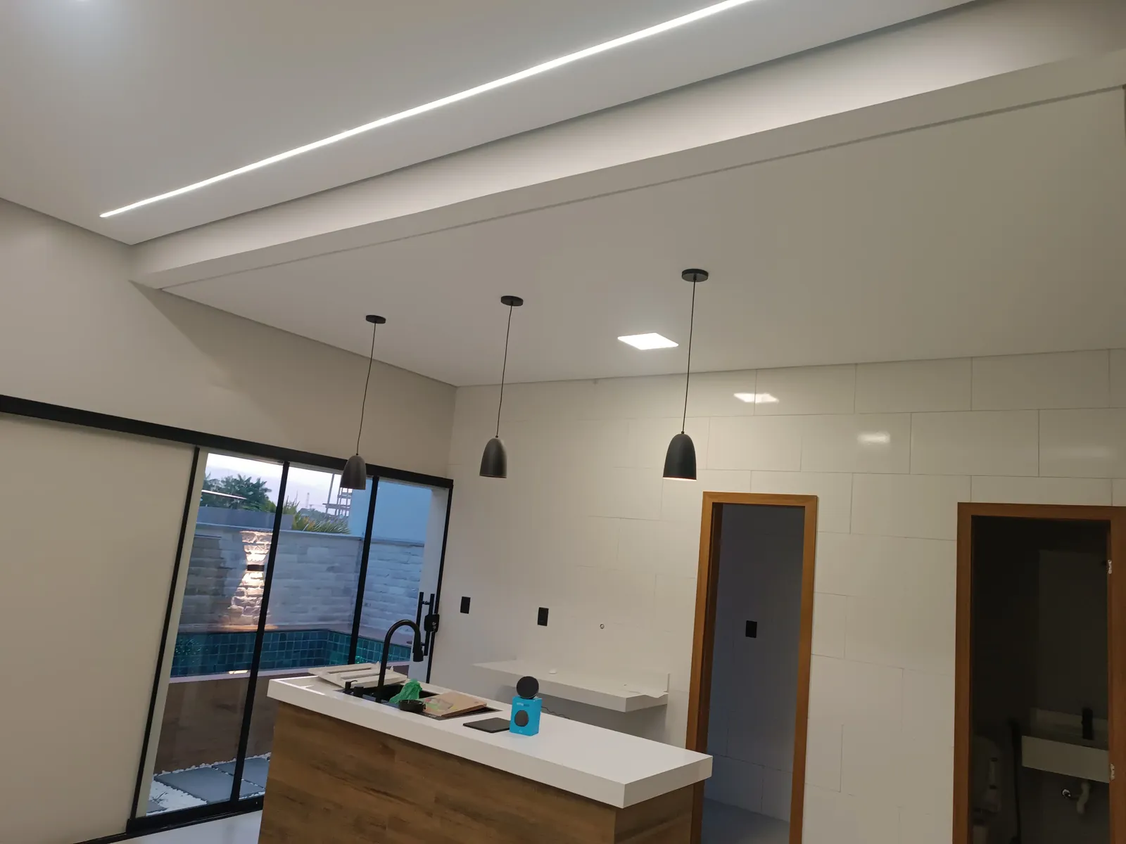 Cozinha com ilha em madeira, pendentes e vista para a piscina