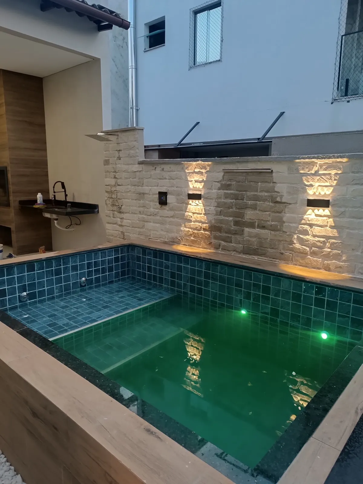 Piscina iluminada ao entardecer, com a bancada da área coberta ao fundo