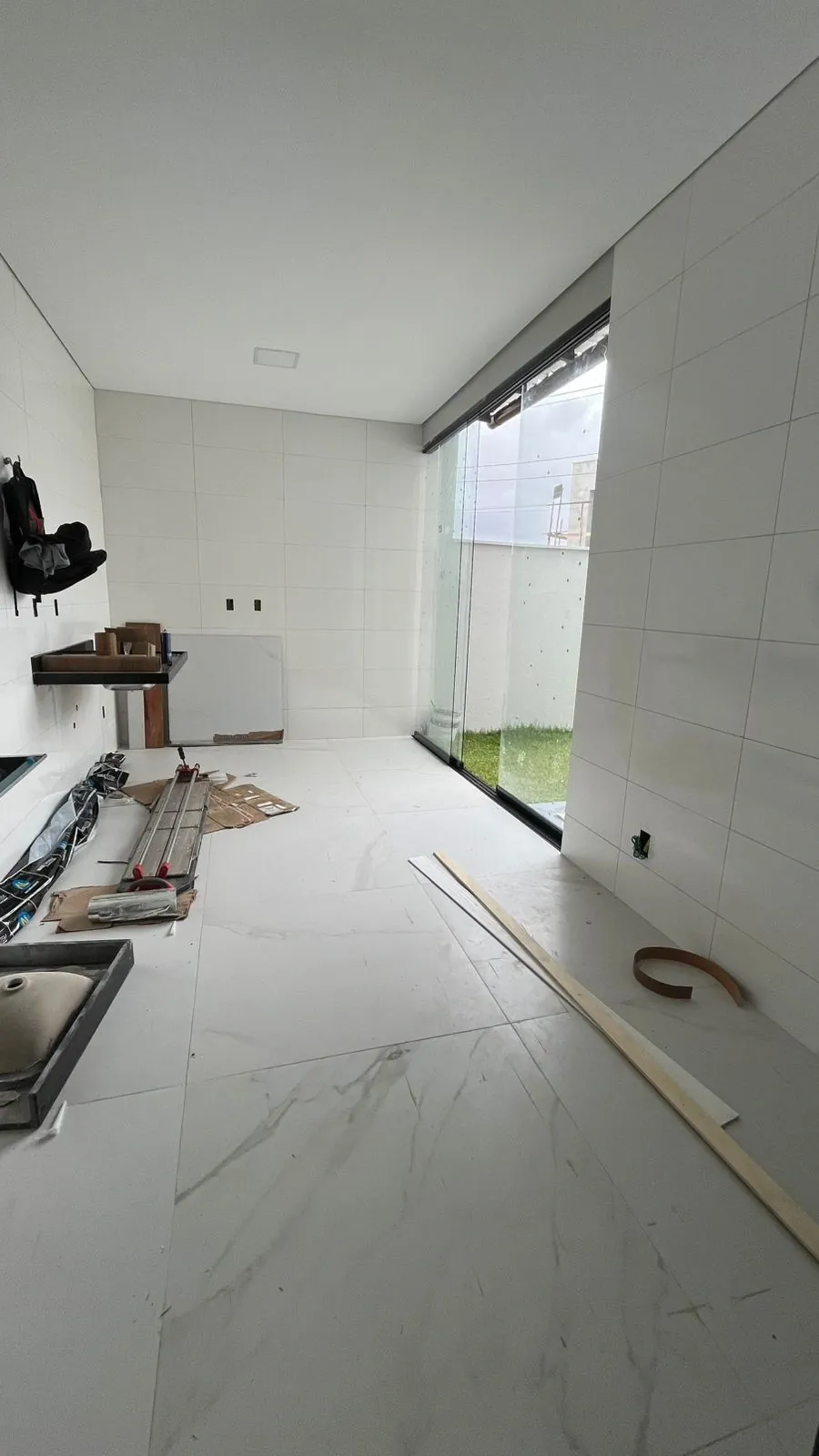 Cozinha na fase de assentamento do porcelanato, com esquadria para o quintal