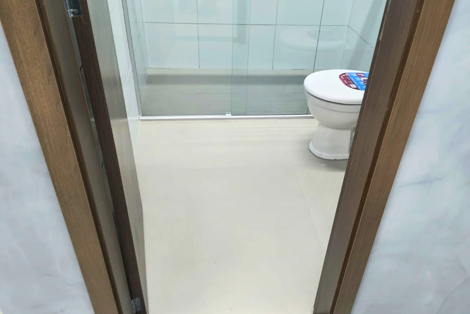 Banheiro visto da porta, com box e porcelanato claro